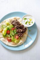Lamb skewers on a pita bread with salad served with a yoghurt sauce garnished with peppermint