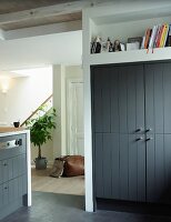 Fitted cupboard with wooden doors painted dark grey below shelf niche and view through open doorway into hall