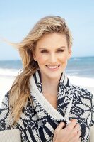 Junge, blonde Frau am Strand mit weiss-blau gemusterter Strickjacke mit Schalkragen