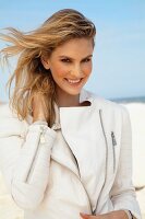 Junge, blonde Frau am Strand mit weisser Lederjacke