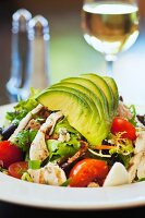 Cobb Salad mit Avocado, Tomaten, Speck und Hähnchen vor einem Glas Wein