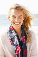 A young blonde woman by the sea wearing a light jumper and a scarf