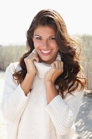 A young brunette woman outside wearing a white knitted roll-neck jumper