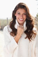 A young brunette woman outside wearing a white knitted roll-neck jumper