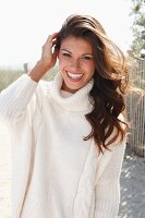 A young brunette woman outside wearing a white knitted roll-neck jumper