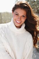 A young brunette woman outside wearing a white knitted roll-neck jumper