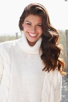 A young brunette woman outside wearing a white knitted roll-neck jumper