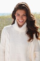 A young brunette woman outside wearing a white knitted roll-neck jumper