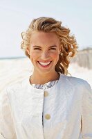 A young blonde woman on a beach wearing a white coat