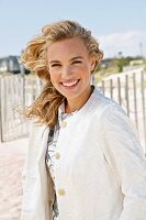 A young blonde woman on a beach wearing a white coat