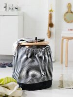 A wooden stool with a homemade, black-and-white striped fabric bag as a laundry basket in a modern bathroom