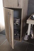 A tall, oak-effect cupboard with stainless steel handles with the lower door open to show towels; floor and wall covered in brown quiet tiles to match the furniture