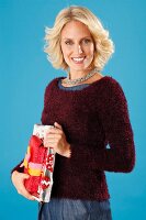 A young blonde woman holding presents and wearing a dark red jumper