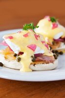 English Muffins mit pochiertem Ei, karamellisierten Zwiebeln, Räucherlachs, Kapern und Sauce Hollandaise