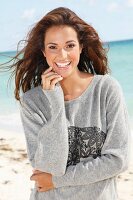 A young brunette woman by the sea wearing a grey sweatshirt
