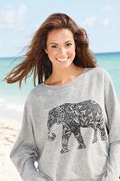 A young brunette woman by the sea wearing a grey sweatshirt with an elephant print
