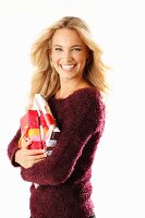 A young blonde woman holding presents and wearing a burgundy knitted jumper