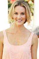 A blonde woman wearing a pink top with her hair tied back