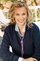 A young blonde woman outside wearing a dark blue knitted jumper and a denim shirt