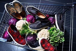 Blick in Einkaufswagen mit verschiedenen Modellen von Sneakers und Gemüse