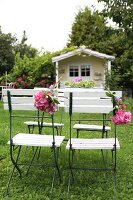 Klappstühle mit Hortensienzweigen dekoriert auf der Wiese, im Hintergrund romantisches pastellgelbes Gartenhäuschen