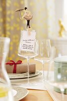 A tightrope walker figure on a clothes peg holding a menu to a wine glass