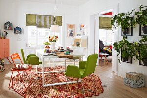 A friendly furnished dining room, green upholstered chairs and folding chairs around a white table on a designer table with flower pots on the wall