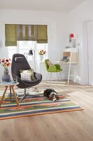 Grauer Sessel mit Nackenrolle und schlichter Beistelltisch auf gemustertem Teppich und Hund im Wohnzimmer