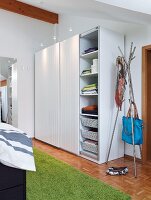 A storage solution on a bedroom consisting of a simple cupboard with sliding doors and spotlights next to a hat stand