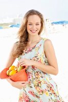 Junge Frau im Sommerkleid hält mit Obst gefüllten Hut