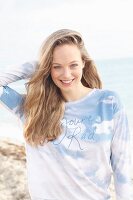 A young blonde woman by the sea wearing a longsleeved T-shirt