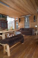 Rustikaler Wohnraum im Chalet, Essplatz mit dunklem Tierfell auf Bank, im Hintergrund gemütliches Sofa vor Glasschiebetür