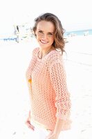 Junge Frau in apricotfarbenem Sommerpulli am Strand
