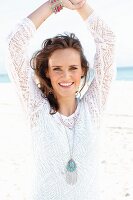 A young, long-haired woman on a beach wearing a white lace dress