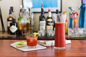 A classic Bloody Mary drink with celery on a table with a home bar in the background