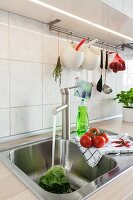 Edelstahl Spülbecken, darüber an Stange aufgehängtes Küchengeschirr in renovierter Küche