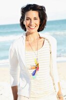 A dark-haired woman on a beach wearing a light t-shirt and jacket