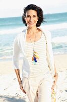 A dark-haired woman on a beach wearing a light t-shirt and jacket