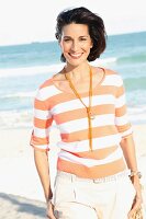 A dark-haired woman on a beach wearing a striped top