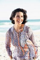 A dark-haired woman on a beach wearing a patterned blouse