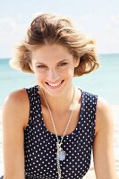 A young blonde woman on a beach wearing a sleeveless, polka-dot summer dress