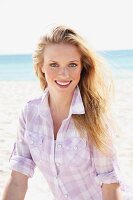 A young blonde woman on the beach wearing a purple and white checked blouse