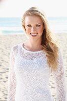 Junge blonde Frau in weißem Top und transparentem Strickpulli am Strand
