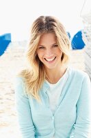 A young blonde woman on a beach wearing a light blue shirt and cardigan