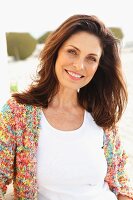 A brunette woman on a beach wearing a white top and colourful cardigan