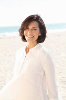 A brunette woman on a beach wearing a thin white blouse