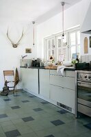 Modern kitchen counter below window and antlers hung on wall of rustic kitchen; tiled floor with dark accent tiles