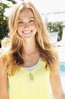 A blonde woman wearing a light yellow top and fashionable necklace