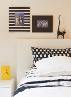 Mixture of black and white patterns on pillow covers, decorative picture frames and cat ornament on bed headboard