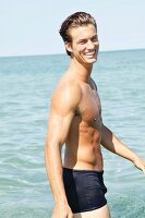A muscular young man by the sea wearing blue bathing shorts